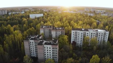 İHA, terk edilmiş Pripyat şehrinden geçiyor. Yıkılmış binalar. Şehrin aşırı gelişmiş caddeleri. Sonbahar renkleriyle Çernobil Hava Aracı Videosu - Günbatımı