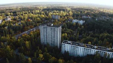 İHA, terk edilmiş Pripyat şehrinden geçiyor. Yıkılmış binalar. Şehrin aşırı gelişmiş caddeleri. Sonbahar renkleriyle Çernobil Hava Aracı Videosu - Günbatımı