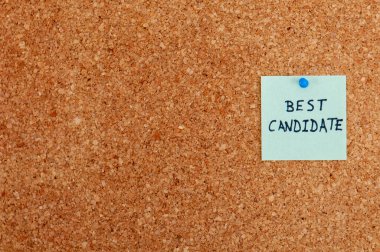 Bir mantar panoda mavi bir raptiyeyle emniyete alınmış soluk yeşil yapışkan bir not var. Siyah mürekkeple yazılmış 