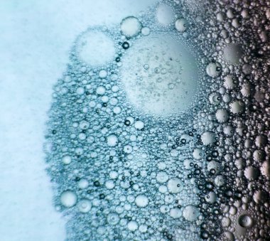 Soyut makro fotoğraf, suda asılı duran yağ baloncuklarını yakalar ve açık mavi eğimli arkaplanda karmaşık dairesel desenler yaratır. Kabarcıklar boyutları ve yoğunlukları değişerek organik ve dokulu bir yapı oluştururlar. Bu yakın plan resim yüksekliği