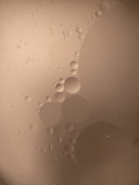 Makro fotoğraf, yumuşak bej arka planda suyun içinde asılı duran çeşitli boyutlarda sayısız yuvarlak yağ kabarcıklarını gösteriyor. Şeffaf kabarcıklar, yağ ve suyun etkileşimini vurgulayan, soyut ve rüya gibi bir desen yaratıyor. Görüntü bir dakika sunar.