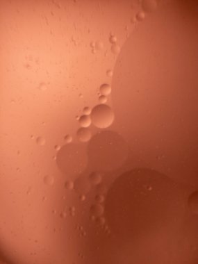 Turuncu arka planlı suda yüzen çeşitli yağ baloncuklarının soyut yakın plan görüntüsü. Makro çekim yumuşak, rüya gibi bir etki yaratıyor. Yumuşak eğimli ve küresel şekilli. Bu da onu bilimsel, sanatsal veya kavramsal kullanım için ideal kılıyor. N