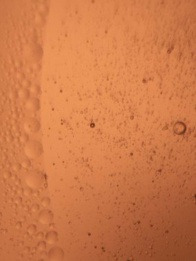 Makro fotoğraf, turuncu bir sıvıda asılı sayısız baloncuğun yakın çekimini gösteriyor. Kompozisyon, değişken kabarcık boyutları ve sıcak, tek renkli turuncu tonu olan soyut bir kalıp yaratıyor..