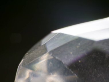 Ayrıntılı bir makro fotoğraf, şeffaf değerli taşın kenarlarını gösteriyor, karmaşık kesikler ve yansımalar görülebilir. Mücevher kısmen bulanık, karanlık ve bulanık bir arkaplana karşı temiz ve parlak yönlerini vurguluyor.