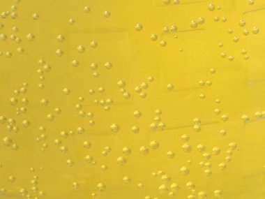 Makro fotografta çok sayıda kabarcığın canlı sarı karbonatlı bir sıvıda asılı olduğu görülüyor. Yükselen kabarcıklar içecek, içecek veya bilim kavramları için uygun soyut, dokulu bir arkaplan oluşturur..