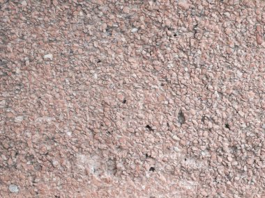 Close-up view of a rough pink exterior wall with small pebble stones embedded in concrete, showing a coarse, textured surface ideal for backgrounds or design elements. The image highlights the unique color and irregular patterns