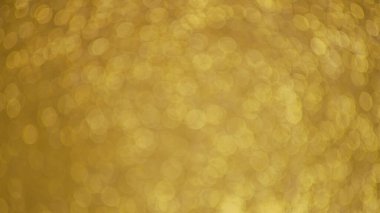 Yumuşak dairesel ışık desenleri içeren altın soyut bir bokeh arka plan. Görüntü, kutlama, bayram veya etkinlik tasarımları için ideal, şenlikli ve zarif bir zemin hazırlayan ılık sarı bir renkle odak dışı..