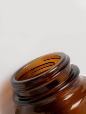 Boynunun detaylı bir makro görüntüsü ve boş bir kehribar kahverengi cam şişenin açılışı. Şişe, pürüzsüz cam dokusunu ve yuvarlak dudağı vurgulayarak, genelde ilaç, takviye veya laboratuvar malzemelerinde kullanılan temiz beyaz arka plana dayanır.