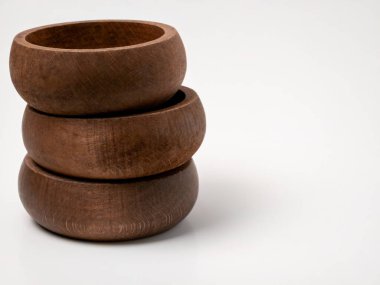 Üç pürüzsüz, yuvarlak ahşap kase, temiz beyaz arka plana karşı düzgünce üst üste istiflenmiş. Doğal ahşap buğday ve sıcak kahverengi renk kâselere mutfak ve yemek kavramları için modern ama kırsal bir estetik veriyor..