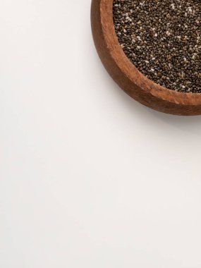 Yuvarlak ahşap bir kasedeki chia tohumlarının temiz beyaz bir zemin üzerine yerleştirilmiş geniş bir kopya alanı var. Görüntü sağlıklı beslenme, organik gıda ve çok yönlü kullanımlar için minimalist gıda sunumunu vurgular.