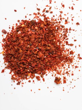 Temiz beyaz bir yüzey üzerinde ezilmiş kırmızı biber taneciklerinin olduğu bir yığına yaklaş. Baharatın dokusu, rengi ve baharatlı doğası görsel olarak vurgulanmış, bu da onu mutfak, yemek ve baharatla ilgili konular için uygun hale getiriyor..