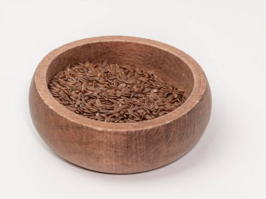 Yuvarlak bir ahşap kaseyi dolduran kahverengi keten tohumu yakın plan temiz beyaz arka planda yakalanır. Görüntü keten tohumlarının dokusunu ve doğal rengini vurgular, besin ve sağlık konsepti olarak görsel olarak uygundur..