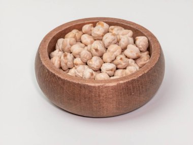 Yuvarlak bir ahşap kaseye yerleştirilmiş kuru nohut fotoğrafı. Kâse, baklagillerin doğal rengini ve dokusunu vurgulayan düz beyaz bir zemine dayanır. Sağlıklı beslenme ya da bitkisel beslenmeyi göstermek için mükemmel..