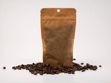 Kahverengi Kraft kağıt kahve poşeti, temiz beyaz arka planda dağınık kahve çekirdekleri ile çevrili olarak ayakta duruyor. Kese markasız ve kahve veya sürdürülebilir ambalaj içeren ambalaj, marka veya reklam kavramları için idealdir..