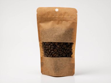 Temiz beyaz arka planda sergilenen kavrulmuş kahve çekirdekleri ile dolu bir stand-up kese. Kese içinde koyu kahve çekirdeklerini gösteren şeffaf bir pencereye sahiptir. Markalaşma, paketleme veya reklam kavramları için uygundur..