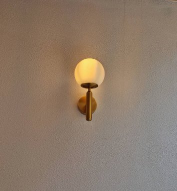 Sarı altın renkli lamba duvarda asılı. Işığı odayı aydınlatıyor.