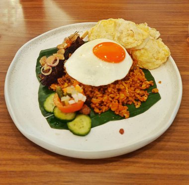 Jakarta, Endonezya - 20 Aralık 2024: Beyaz bir tabakta servis edilen kızarmış yumurta, salatalık turşusu ve krakerlerle birlikte kızarmış pirinç