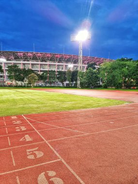 Jakarta, Endonezya - 20 Ocak 2025: Parlak projektörlerle aydınlatılmış atletizm merkezi olarak işaretlenmiş kırmızı koşu pisti