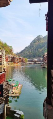 Zhangjiajie, Çin - Nisan 07, 2025: Fenghuang Antik Kenti 'nin büyüleyici manzarası Diaojiaolou olarak bilinen geleneksel stilt evlerden, dekore edilmiş teknelerden, liman manzarasından, çok katmanlı pagoda kulesinden ve yemyeşil yamaçtan oluşuyor