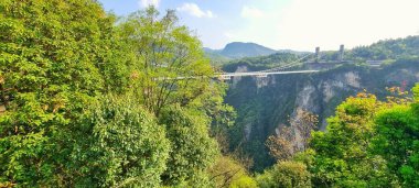 Zhangjiajie, Çin - 10 Nisan 2025: Şeffaf cam yüzeyi ile asma köprü doğrudan aşağıdaki kanyonun dağlık arazisini görmek için