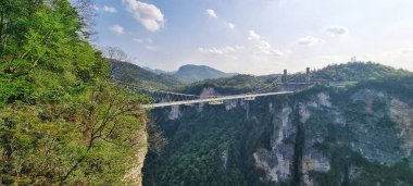 Zhangjiajie, Çin - 10 Nisan 2025: Şeffaf cam yüzeyi ile asma köprü doğrudan aşağıdaki kanyonun dağlık arazisini görmek için