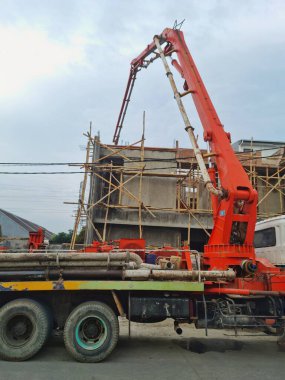 Bandung, Endonezya - 3 Mayıs 2025: İnşaat alanına sıvı beton pompalamak için uzun eklemli kollu büyük beton pompa kamyonu yukarı doğru genişletilir