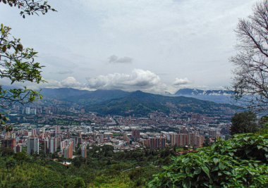 Bulutlu bir günde dağın tepesinden şehir manzarası ve arka planda dağlar.