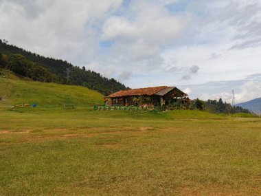 Çiftlikteki ev tuğla renkli çamur çatısı, koridorda çiçekler, gökyüzü bulutları, yeşil dağlarla çevrili