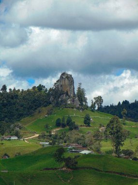 Dağların ortasında tırmanmak için büyük bir kaya manzarası ve yeşil çimenler, bulutlu güneşli bir gün.