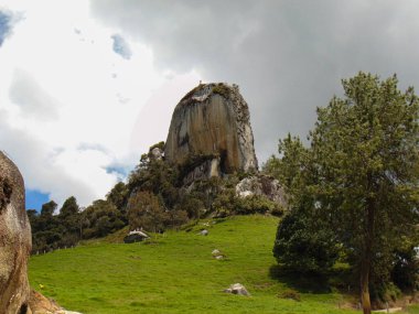 Dağların ortasında tırmanmak için büyük bir kaya manzarası ve yeşil çimenler, bulutlu güneşli bir gün.