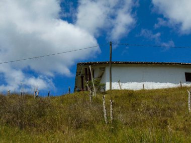 Dağın tepesinde kahverengi çatılı beyaz bir kulübe. Bereketli yeşil otlar ve mavi gökyüzü olan dağ