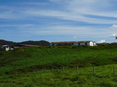 Dağın tepesinde kahverengi çatılı beyaz bir kulübe. Bereketli yeşil otlar ve mavi gökyüzü olan dağ