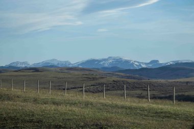 Çitleri olan yuvarlanan tepeler ve arka planda yuvarlanan dağlar.