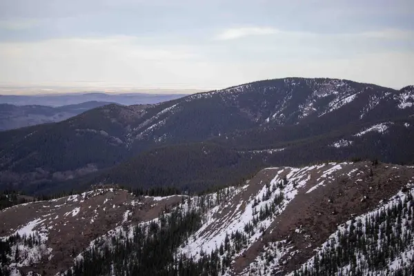 stock image Large mountains with patches of snow and few pine trees, surrounded by vast areas of dirt.