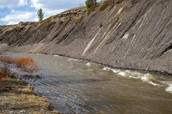 stock image A serene river flows through a rocky landscape, with a steep cliff towering in the background.