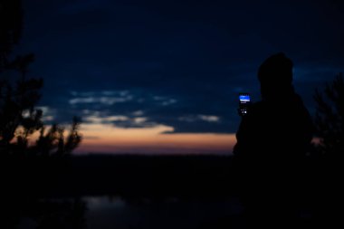 Bir adam gece gökyüzünün fotoğrafını telefonuyla çekiyor. Siluet fotoğraf.