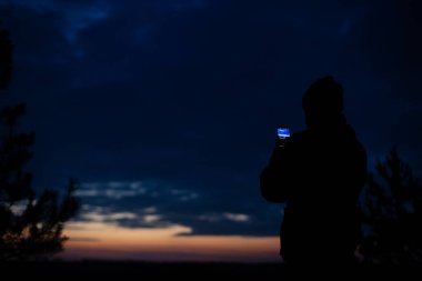 Bir adam gece gökyüzünün fotoğrafını telefonuyla çekiyor. Siluet fotoğraf.