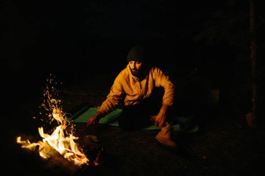 Gezgin gece kamp ateşinin yanında dinleniyor. Gaz lambası ve taşlarla çevrili bir ateşle uyumak için dallardan korunaklı bir barınak..