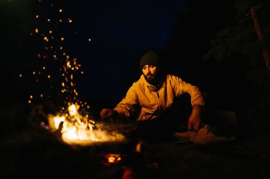 Gezgin gece kamp ateşinin yanında dinleniyor. Gaz lambası ve taşlarla çevrili bir ateşle uyumak için dallardan korunaklı bir barınak..