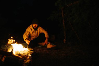 Gezgin gece kamp ateşinin yanında dinleniyor. Gaz lambası ve taşlarla çevrili bir ateşle uyumak için dallardan korunaklı bir barınak..