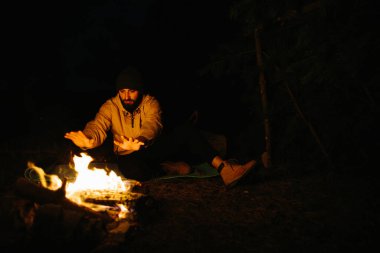 Gezgin gece kamp ateşinin yanında dinleniyor. Gaz lambası ve taşlarla çevrili bir ateşle uyumak için dallardan korunaklı bir barınak..