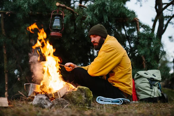 Bearded male hiker roasts sausages on a bonfire. Dinner in the wild, travel and survival concept.