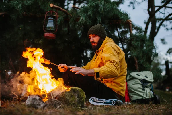髭を生やした男ハイカーはたき火でソーセージをローストします 野生でのディナー 旅行と生存の概念 — ストック写真