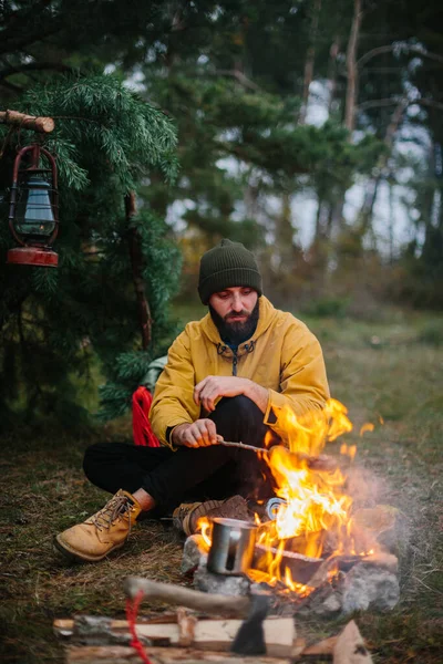 髭を生やした男ハイカーはたき火でソーセージをローストします 野生でのディナー 旅行と生存の概念 — ストック写真