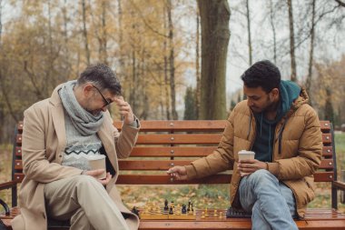 Sonbahar parkında bankta satranç oynayan çok ırklı adamlar..