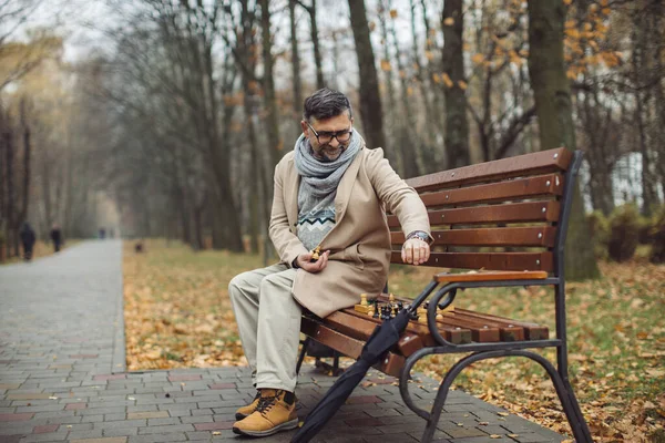 Yaşlı Bir Adam Sonbahar Parkında Bir Bankta Satranç Oynar — Stok fotoğraf
