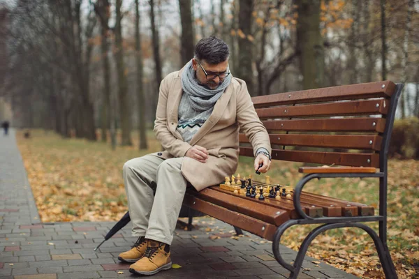 Ένας Ηλικιωμένος Παίζει Σκάκι Ένα Παγκάκι Στο Πάρκο Του Φθινοπώρου — Φωτογραφία Αρχείου