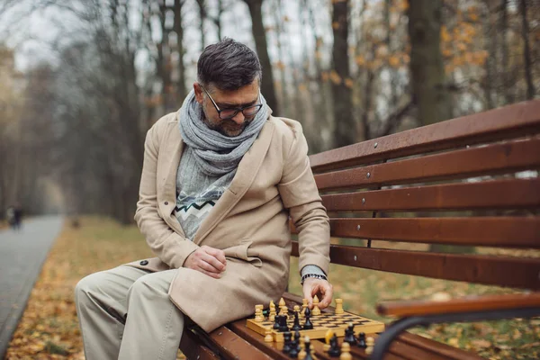 Yaşlı Bir Adam Sonbahar Parkında Bir Bankta Satranç Oynar — Stok fotoğraf