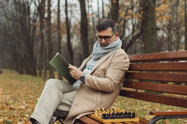 Yaşlı Bir Adam Sonbahar Parkında Bir Bankta Otururken Dergi Okur — Stok fotoğraf
