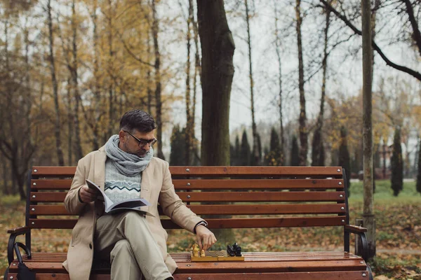 一位老人在秋天公园的长椅上下棋 — 图库照片